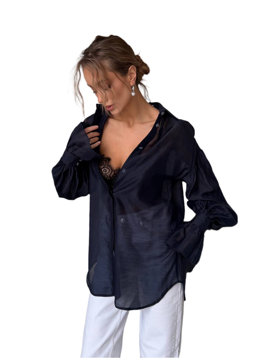 Woman wearing a black sheer blouse over a black top with white pants on a white background