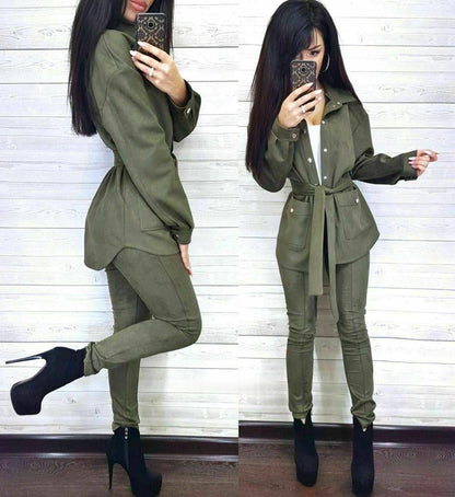 Woman wearing a green outfit with a belt, standing against a white wall.