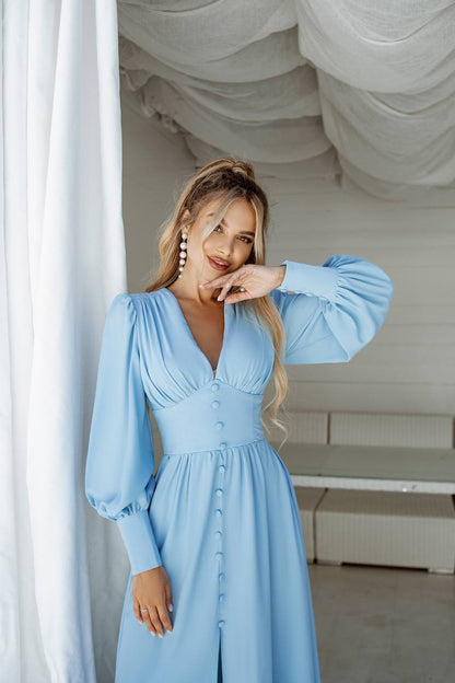 Woman wearing a light blue dress with long sleeves in an indoor setting.