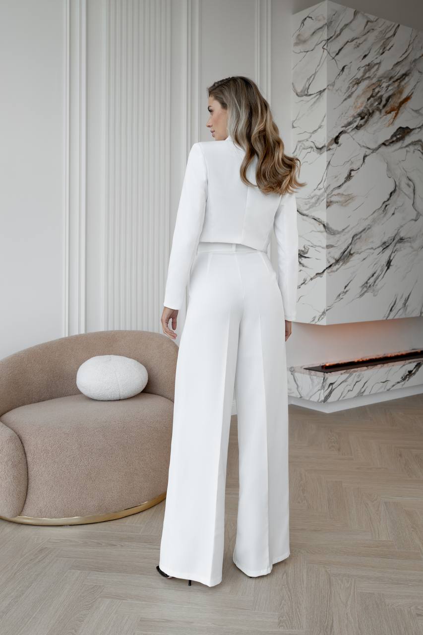 Woman in a white outfit standing in a modern interior setting with a marble wall.