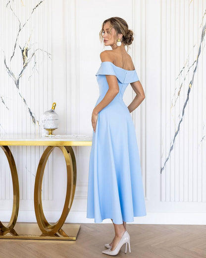 Woman in a light blue off-shoulder dress standing in a stylish room with a gold console table.