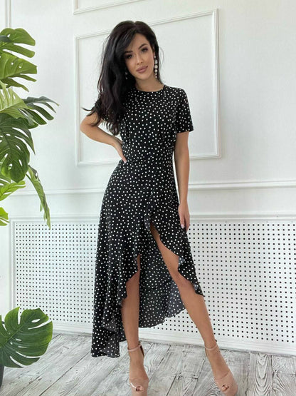 Woman wearing a black polka dot dress in a room with a plant and white wall.