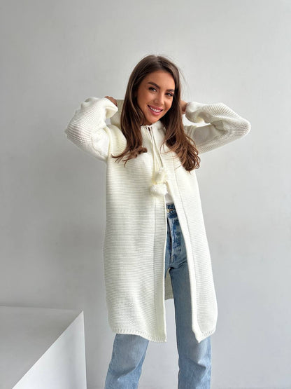 Woman wearing a long cream-colored cardigan over a light blue top and jeans on a plain background