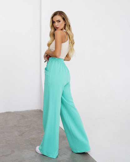 Woman wearing a white top and turquoise pants against a white background