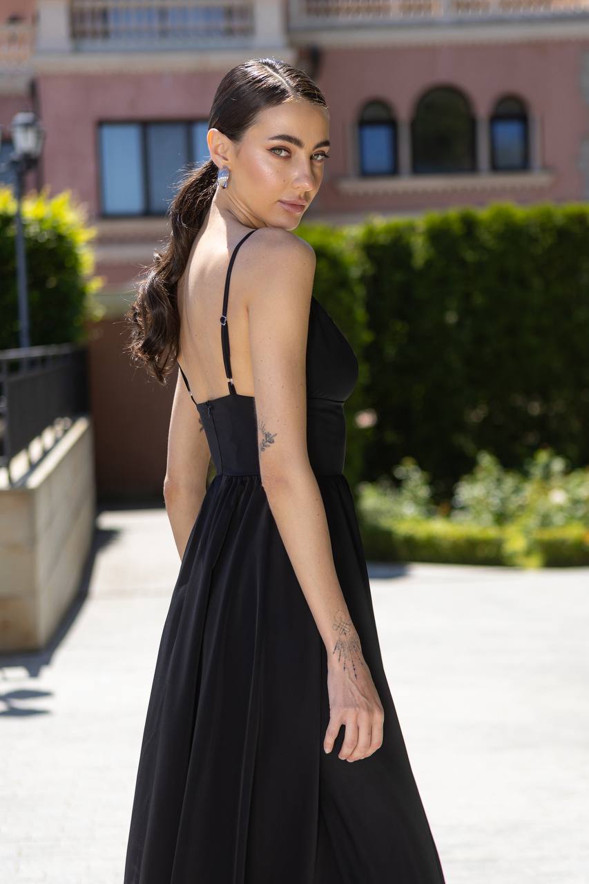 Woman in a black dress standing outdoors with a building and greenery in the background