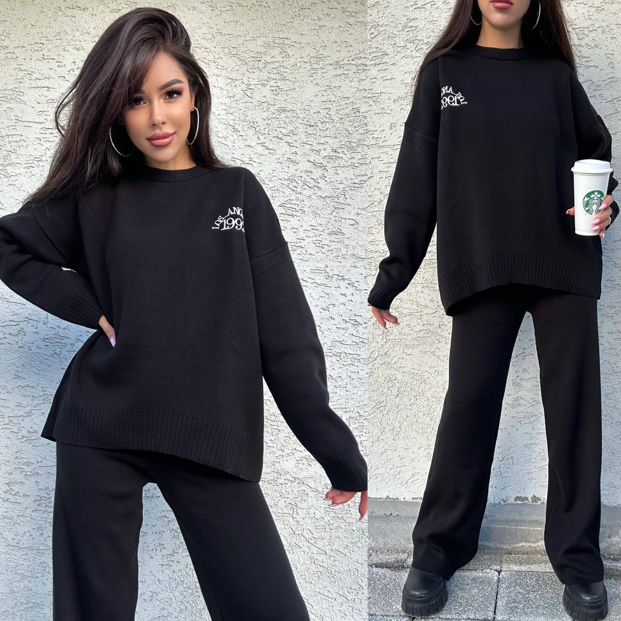 Woman wearing a black outfit with a logo, holding a Starbucks cup against a textured wall.