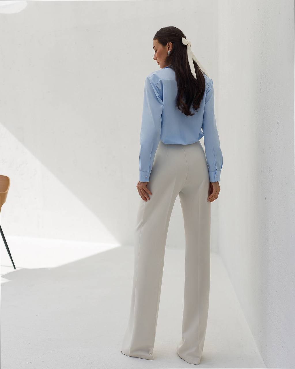 Woman wearing a light blue blouse and beige pants against a white background