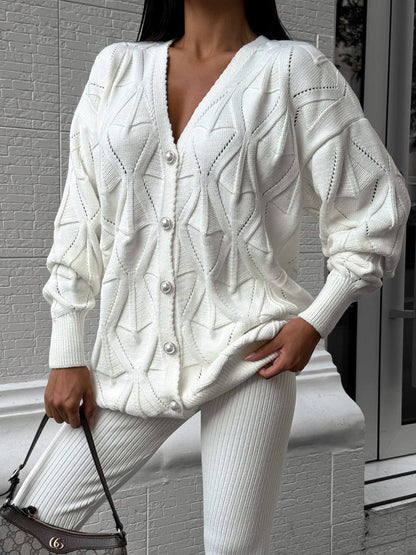 Person wearing a white cable knit cardigan and pants in an indoor setting.