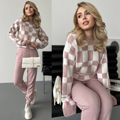 Woman wearing a pink and white checkered sweater and pants sitting on a chair.