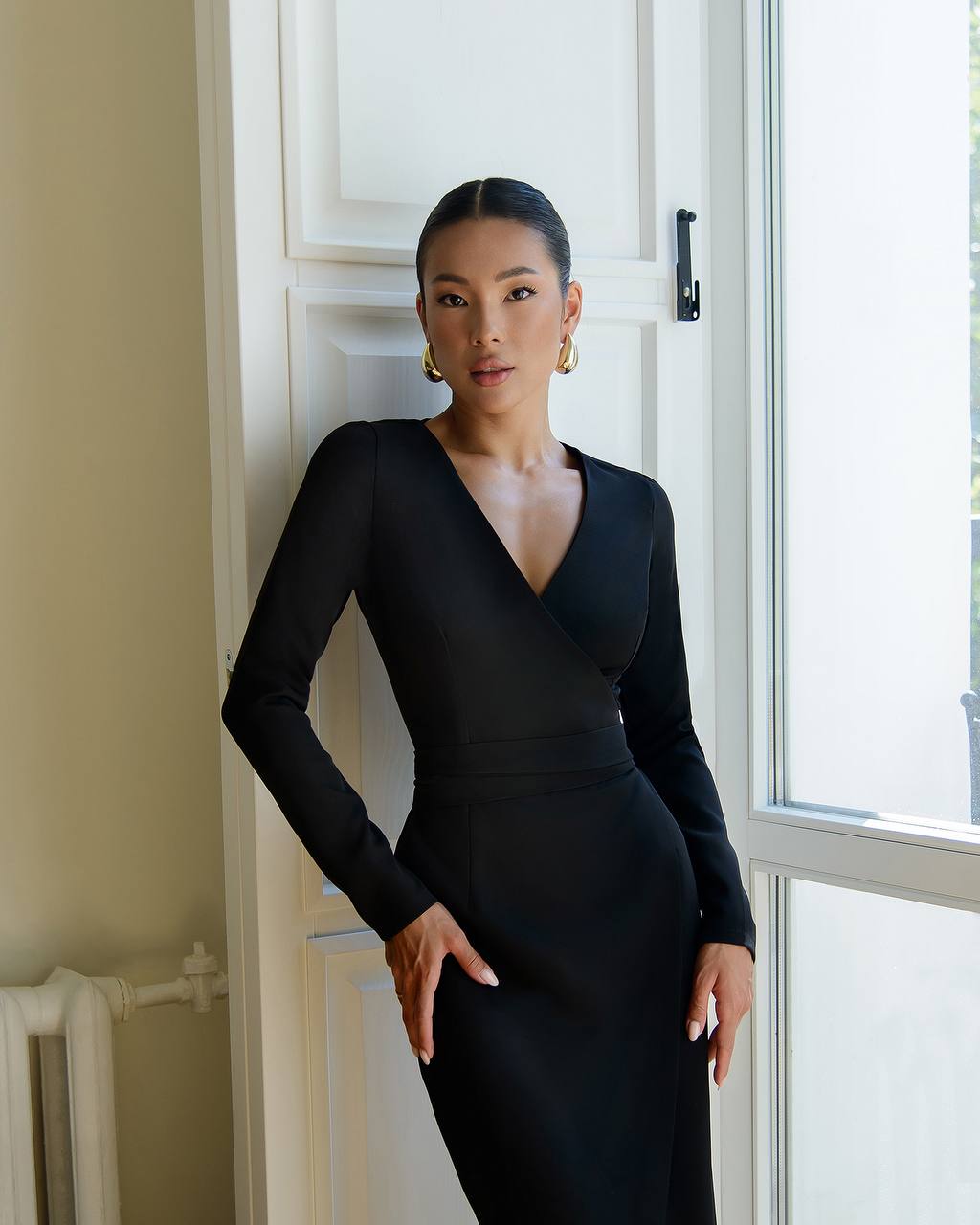 Woman in a black dress standing in a room with a white door and window.