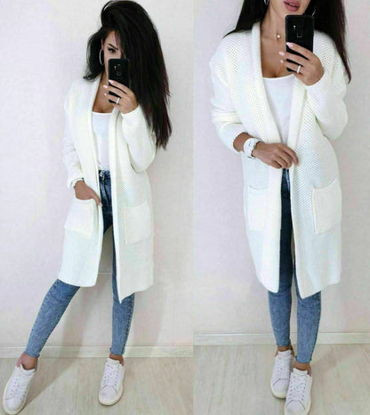 Woman wearing a long white cardigan over a white top and blue jeans, taking a mirror selfie.