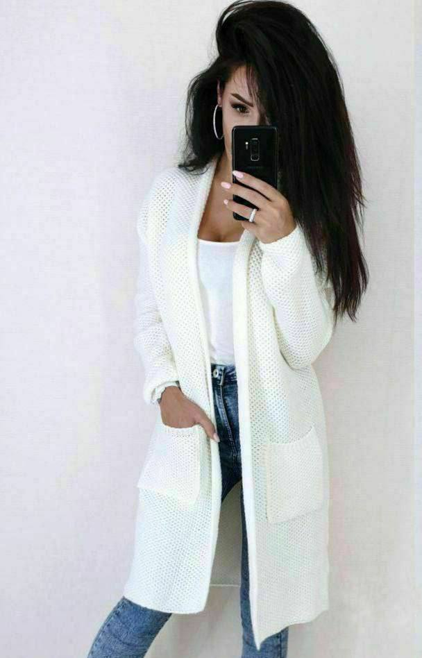Person wearing a white cardigan over a white shirt and blue jeans, taking a mirror selfie.