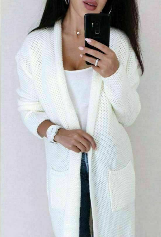 Person wearing a long white cardigan over a white top, holding a phone.