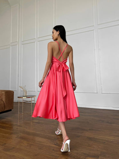 Woman in a pink dress standing in a room with wooden flooring and a white wall.