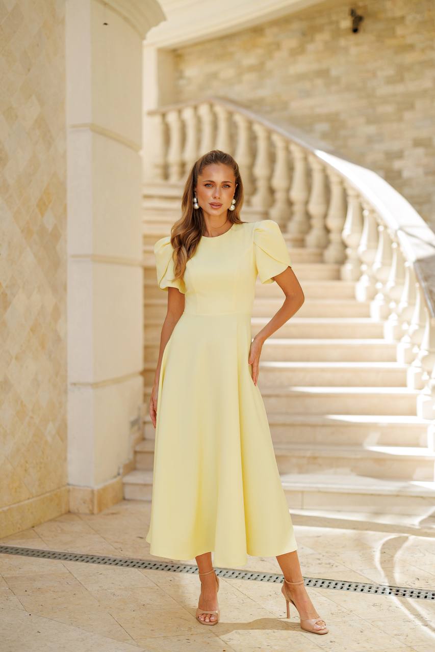 Woman in a yellow dress standing on a staircase with beige walls.
