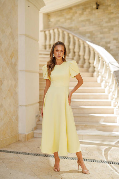 Woman in a yellow dress standing on a staircase with beige walls.