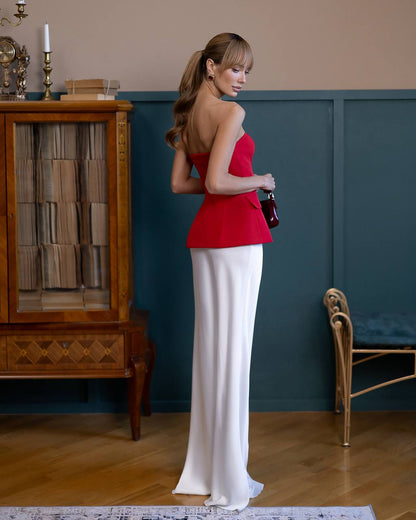 Woman in a red top and white skirt standing in a room with wooden furniture and a blue wall.
