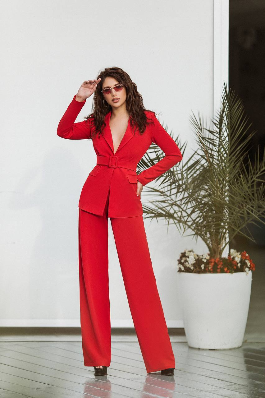 Woman in a red suit standing indoors with a plant in the background
