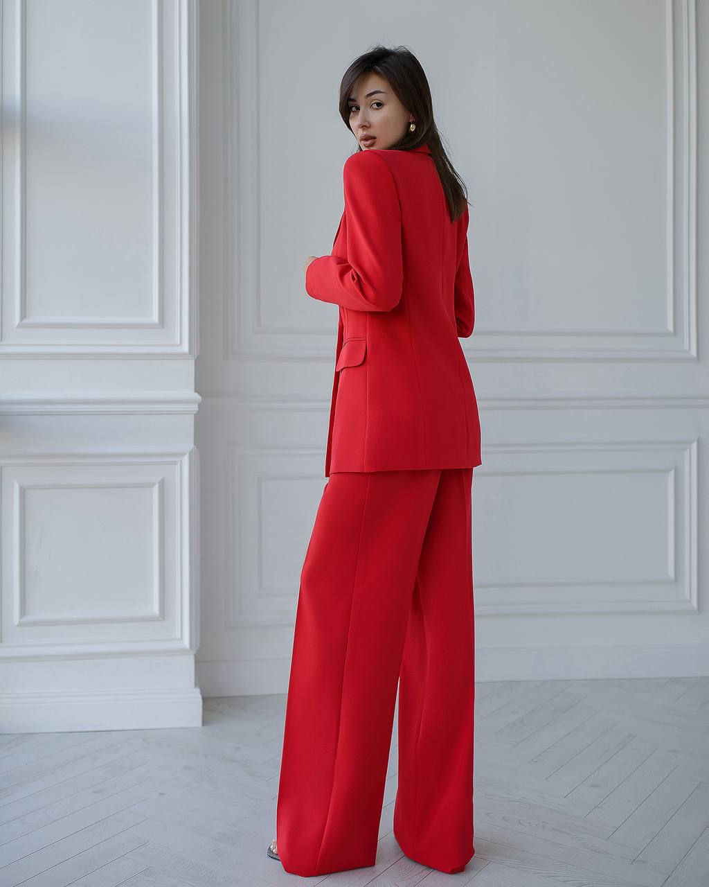 Woman wearing a red suit standing against a white paneled wall.