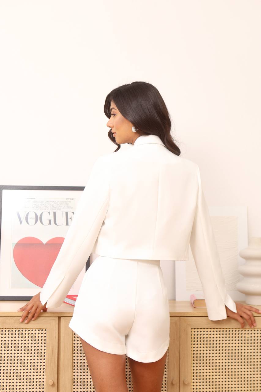 Woman in a white outfit standing in front of a 'Vogue' magazine cover.