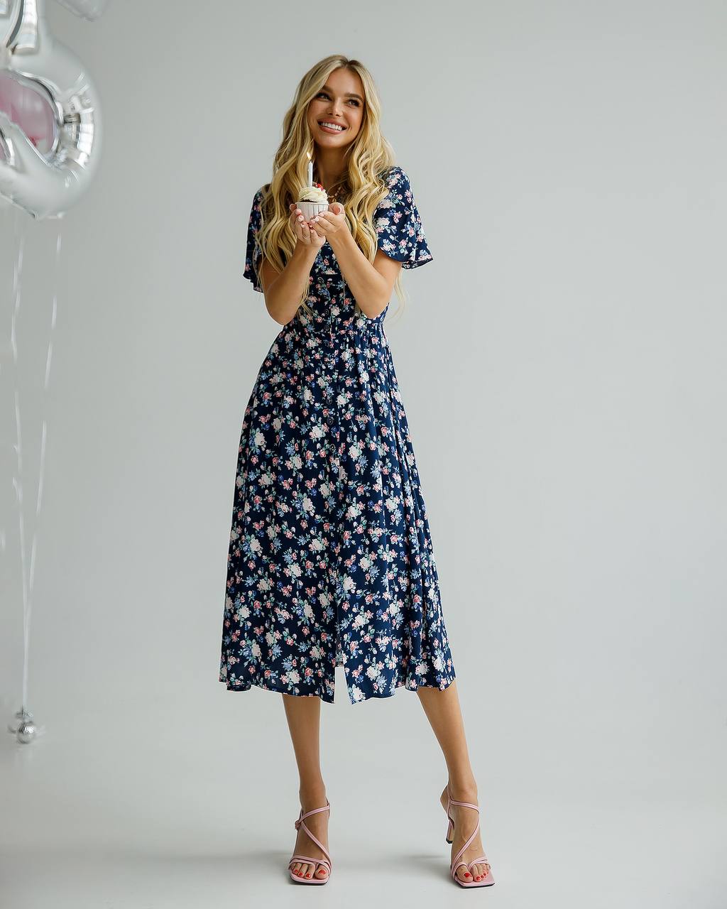 Woman in a floral dress holding a cup against a plain background