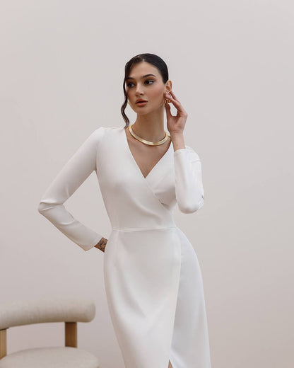 Woman wearing a white dress with long sleeves against a plain background