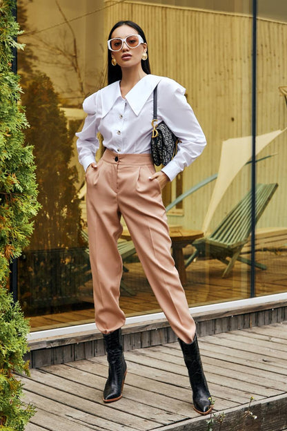 Woman in a white blouse and pink pants standing outdoors near a glass wall.
