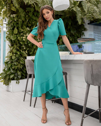 Woman in a teal dress standing in a modern kitchen with greenery.