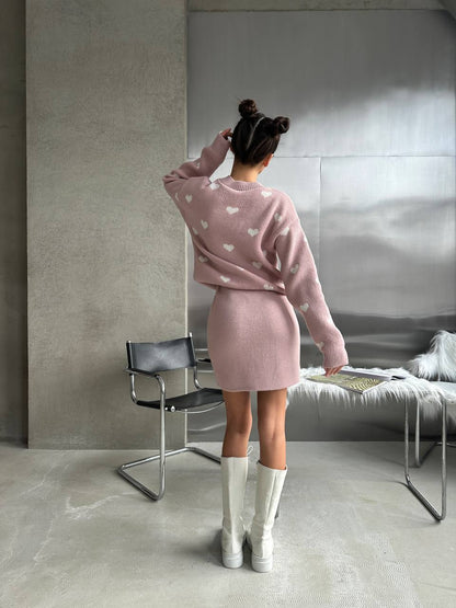 Woman in a pink outfit standing in a minimalistic room with a gray wall and concrete floor.