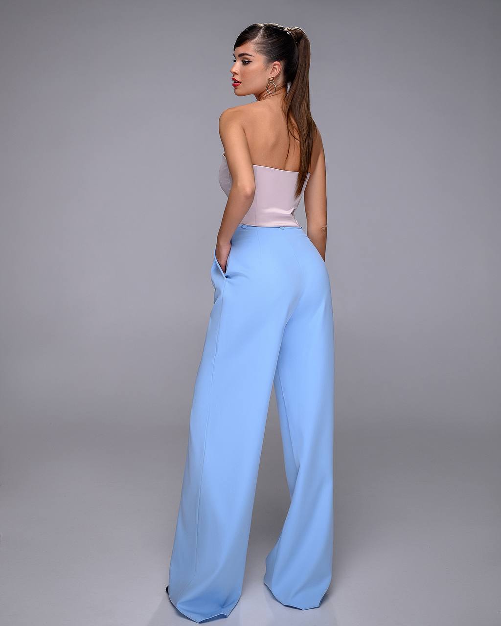 Woman wearing a light pink top and light blue pants against a gray background