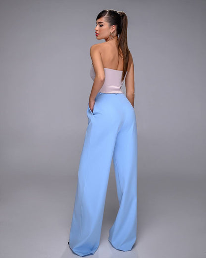 Woman wearing a light pink top and light blue pants against a gray background