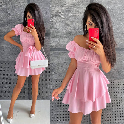 Woman wearing a pink dress with a white handbag against a gray textured wall.