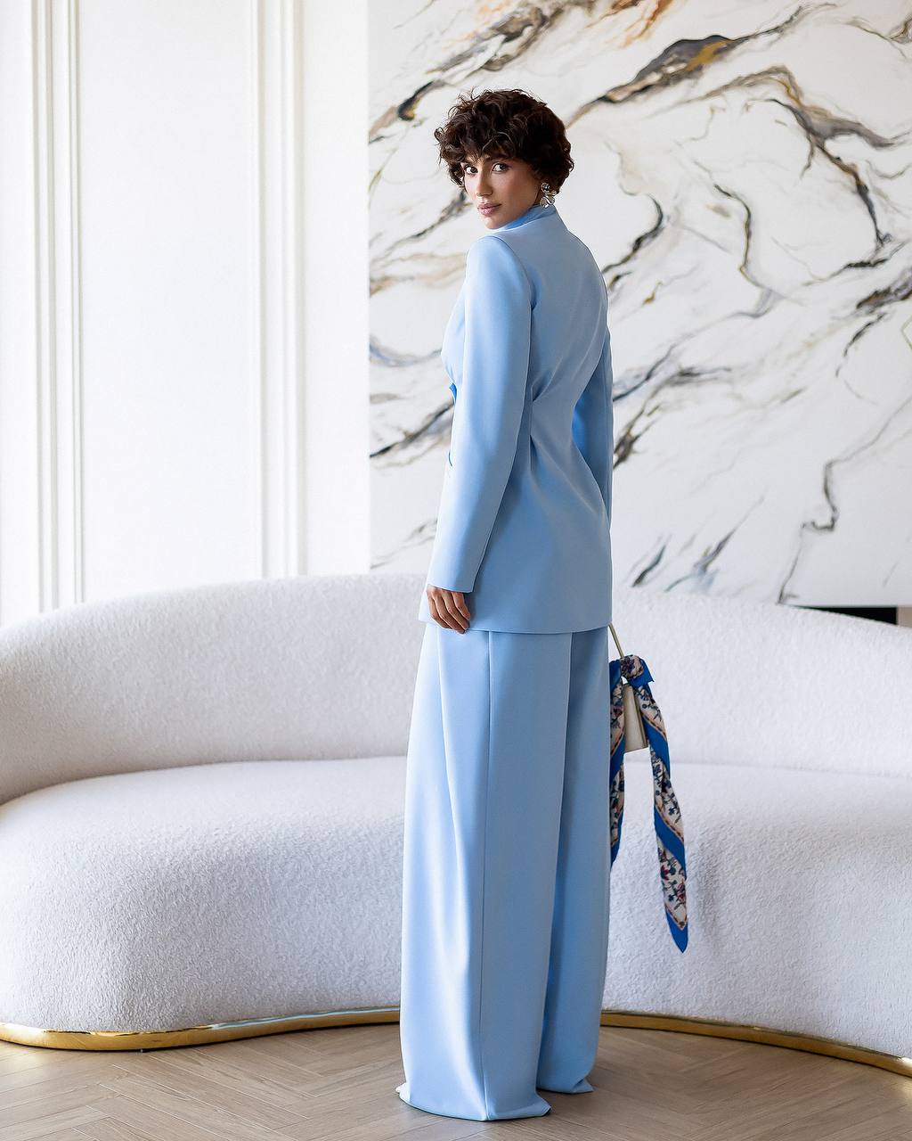 Person wearing a light blue outfit standing in a room with a marble wall.