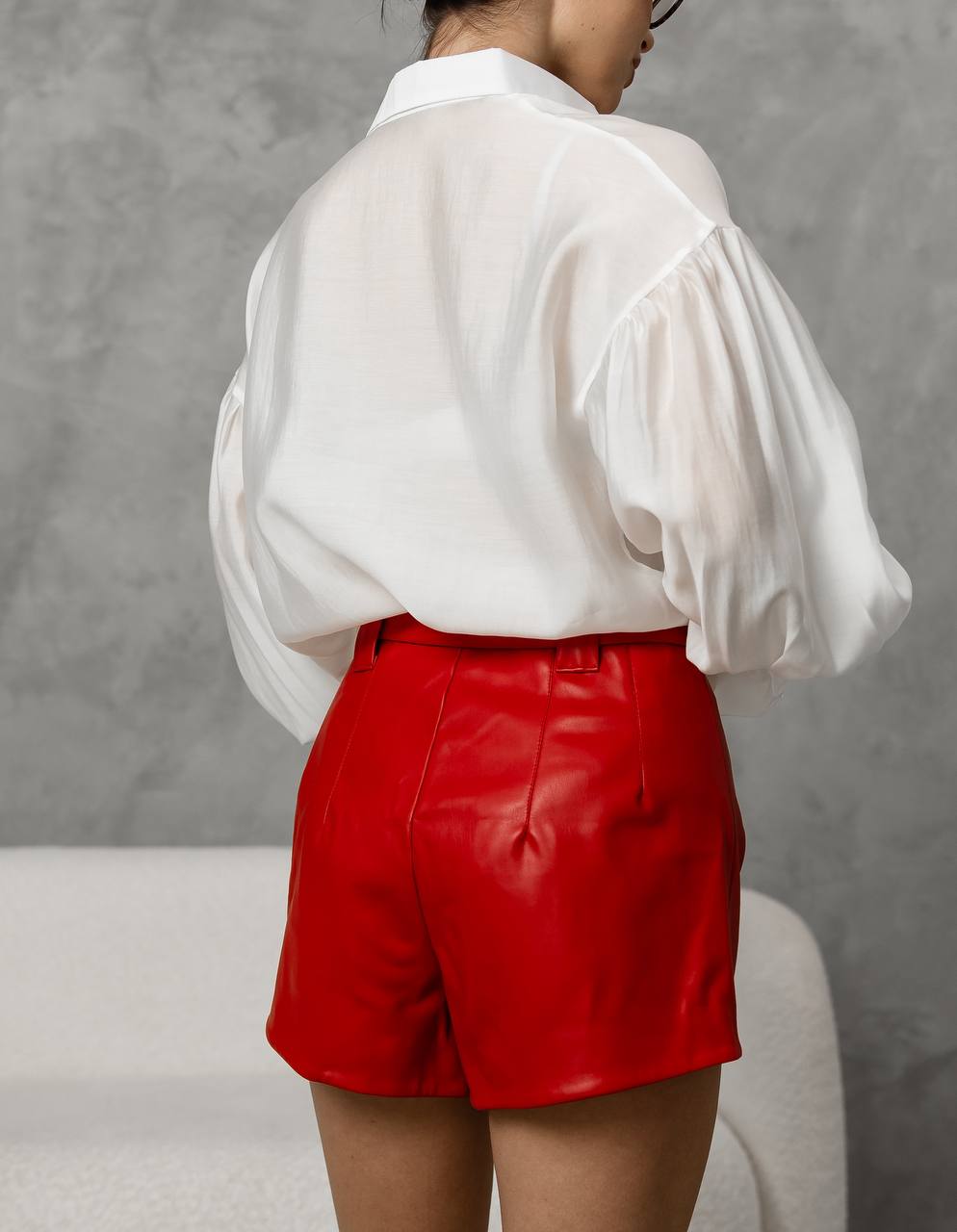 Person wearing a white blouse and red shorts against a gray background