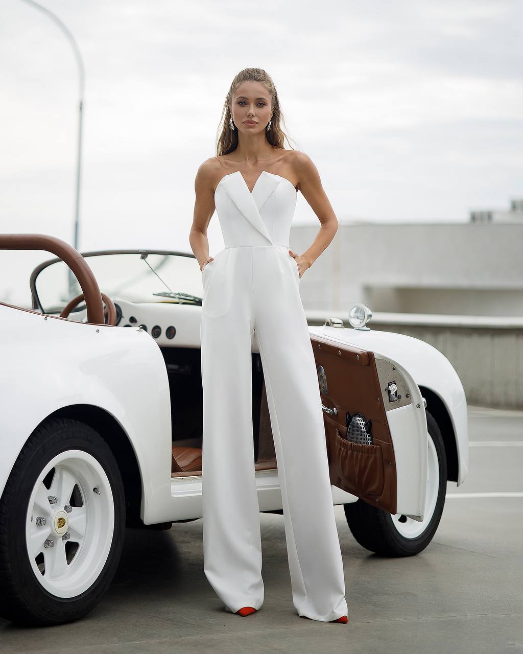 Woman in a white jumpsuit standing next to a vintage car