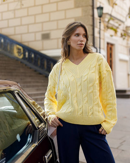 Woman wearing a yellow cable knit sweater standing next to a car on a city street.
