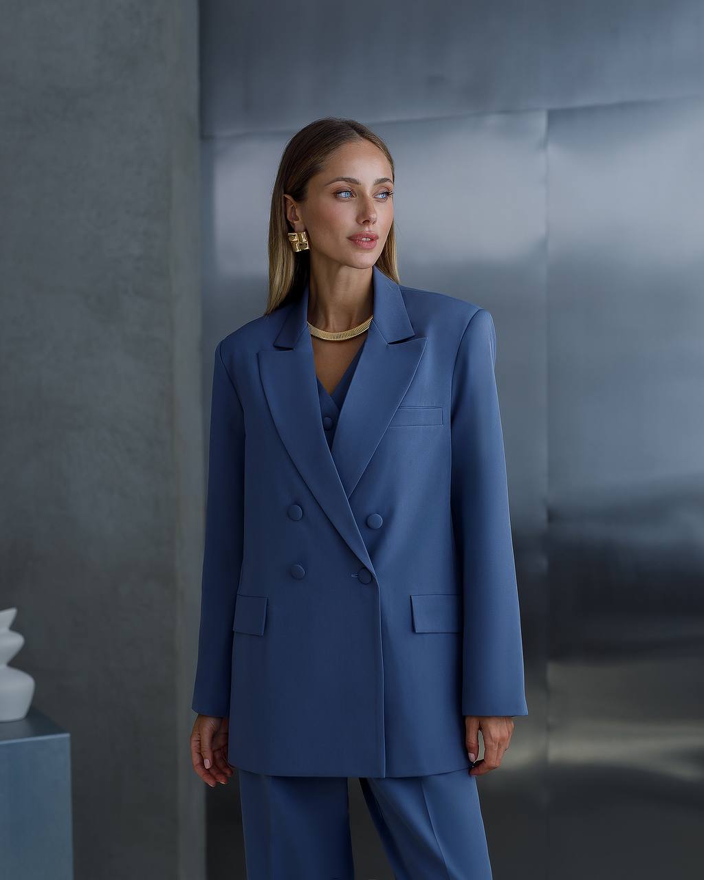 Woman wearing a blue suit standing against a gray wall.