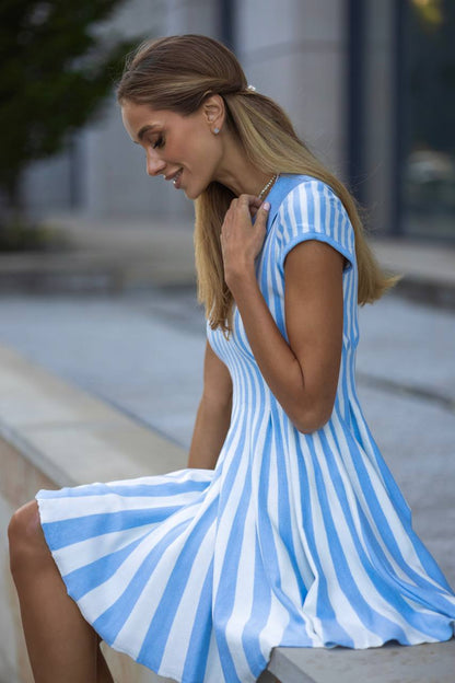 Woman wearing a blue and white striped dress sitting on a bench.