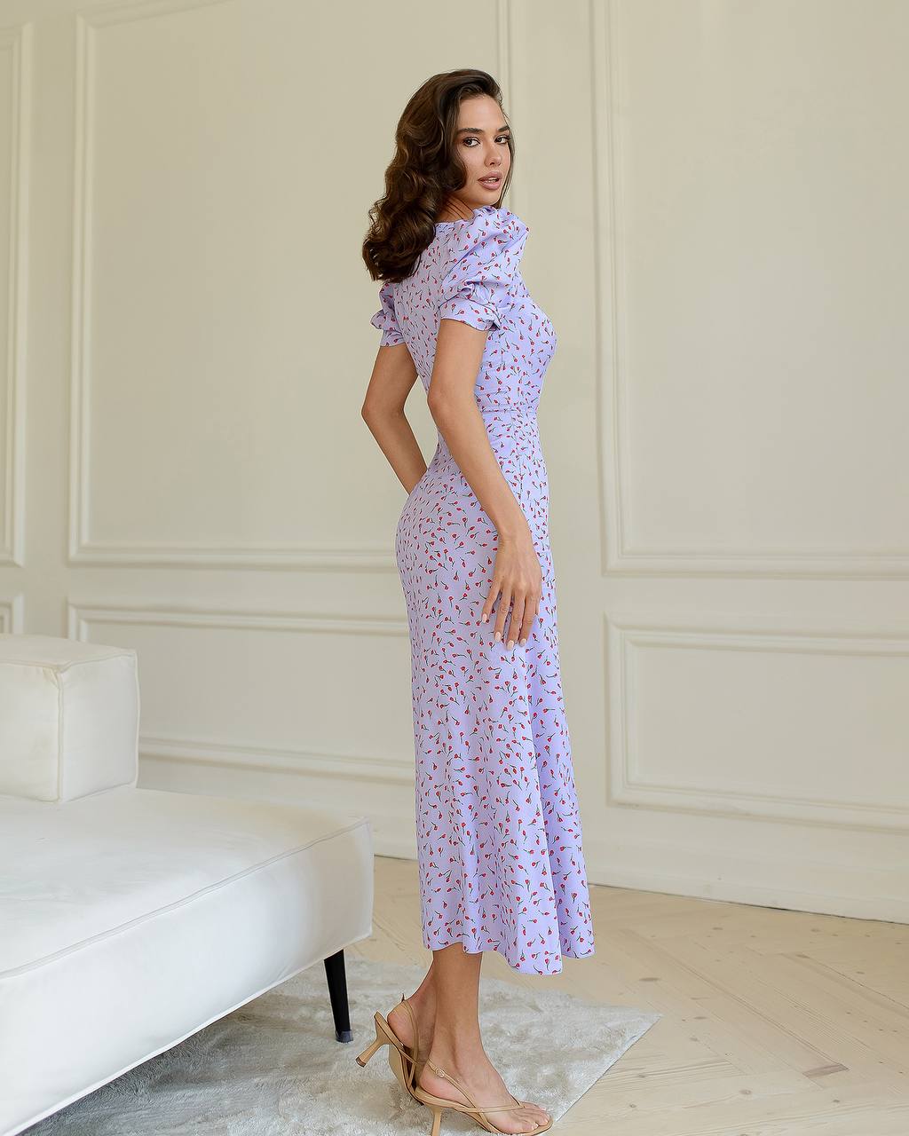 Woman wearing a purple floral dress in a room with white walls and furniture.