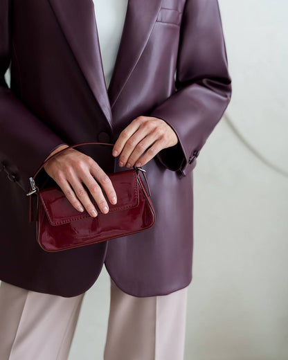 Person wearing a purple blazer holding a red handbag against a neutral background