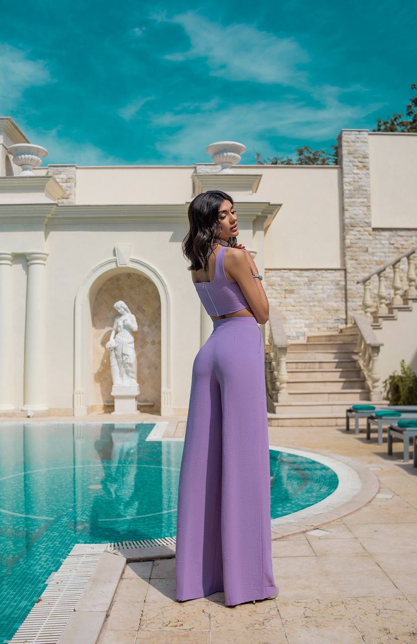 Woman in a purple outfit standing by a pool with a classical building in the background
