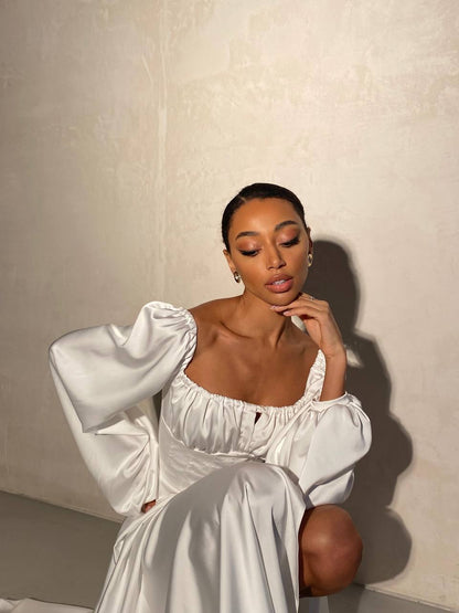 Woman in a white dress sitting against a plain background