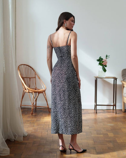 Woman in a patterned dress standing in a room with wooden floor and white walls.