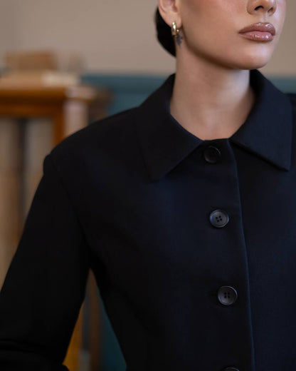 Person wearing a dark blue coat with buttons indoors