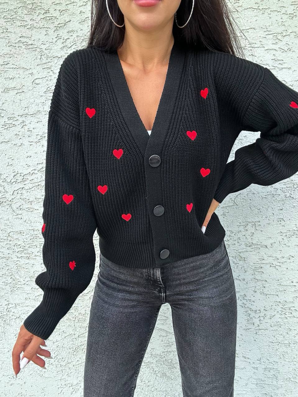 Person wearing a black cardigan with red heart patterns against a light gray background