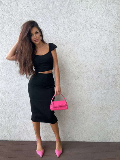 Woman in black outfit holding a pink handbag against a light gray background