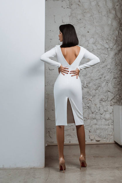 Woman in a white dress with a high slit standing against a textured wall.