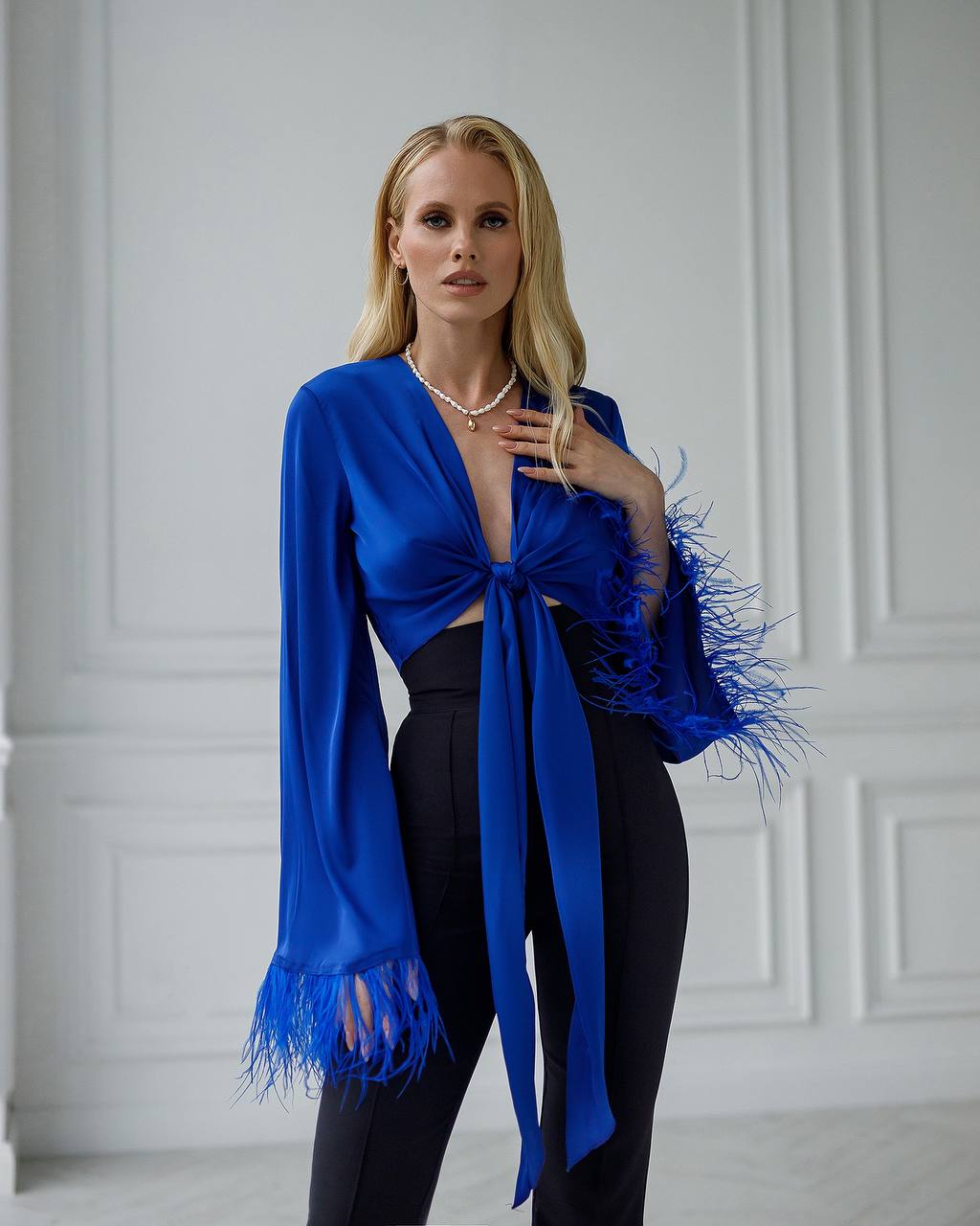 Woman wearing a blue fringed top against a white wall