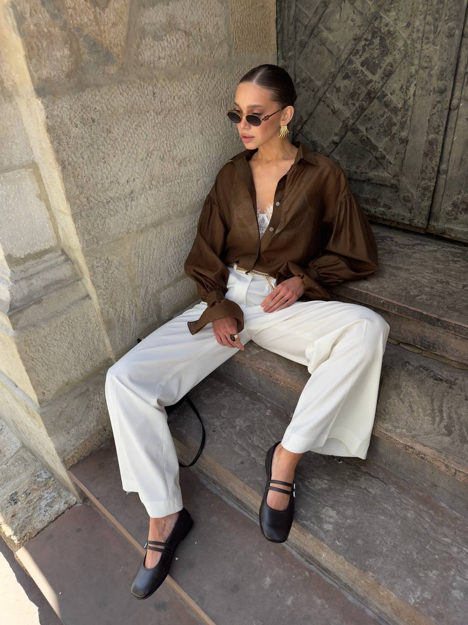 Woman sitting on stone steps wearing a brown shirt and white pants.