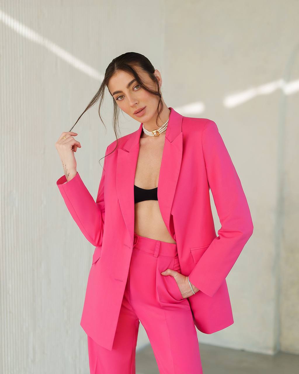 Woman wearing a bright pink suit with a black top against a neutral background